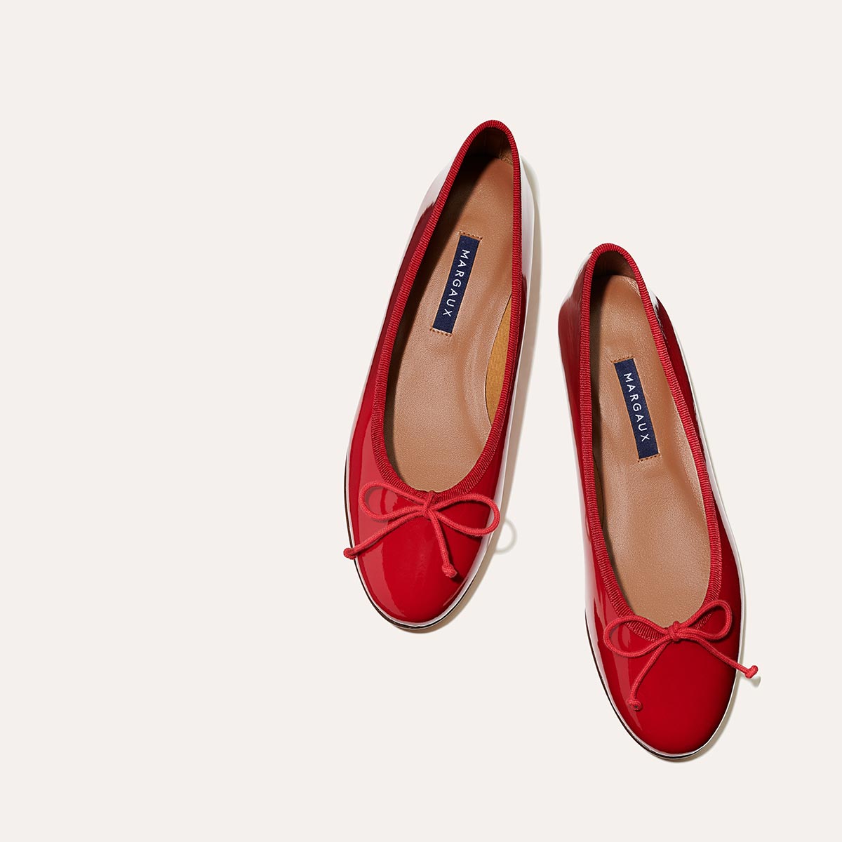 The Demi in Cherry Patent, a comfortable ballet flat with a rounded toe and adjustable cord bow detail.