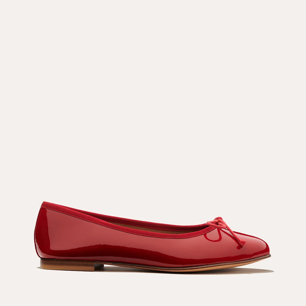 The Demi in Cherry Patent, a comfortable ballet flat with a rounded toe and adjustable cord bow detail.