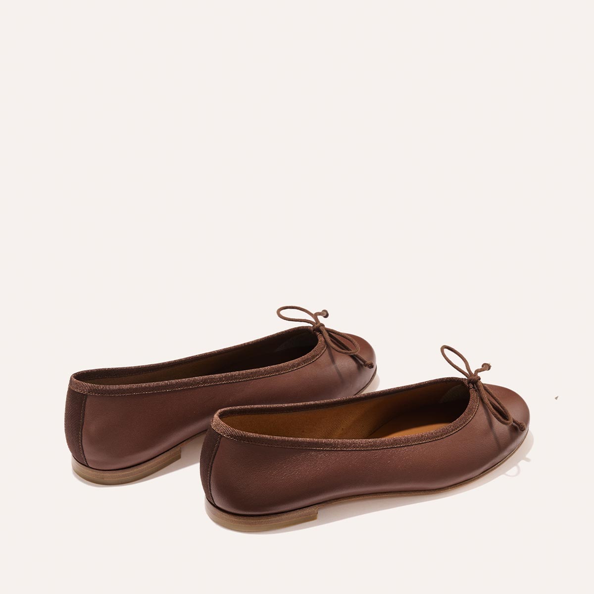 The Demi - Cognac Nappa are comfortable brown leather ballet flats handmade in Spain, featuring a thin bow detail at the toe.