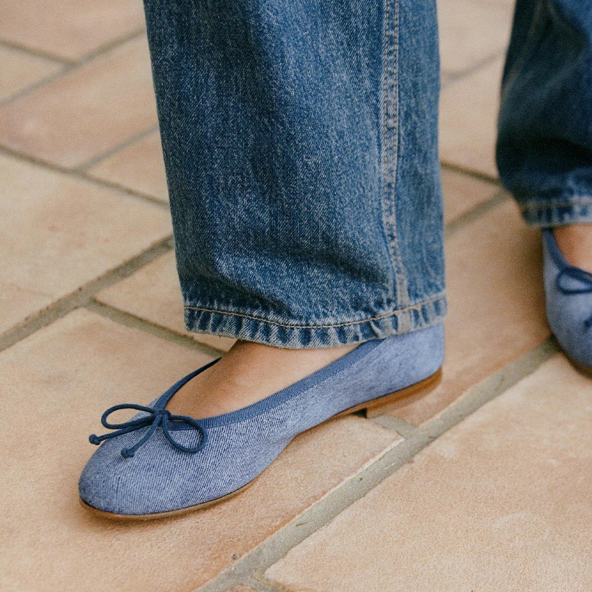 The Demi in soft Denim Suede, a comfortable ballet flat with a rounded toe and adjustable cord bow detail.