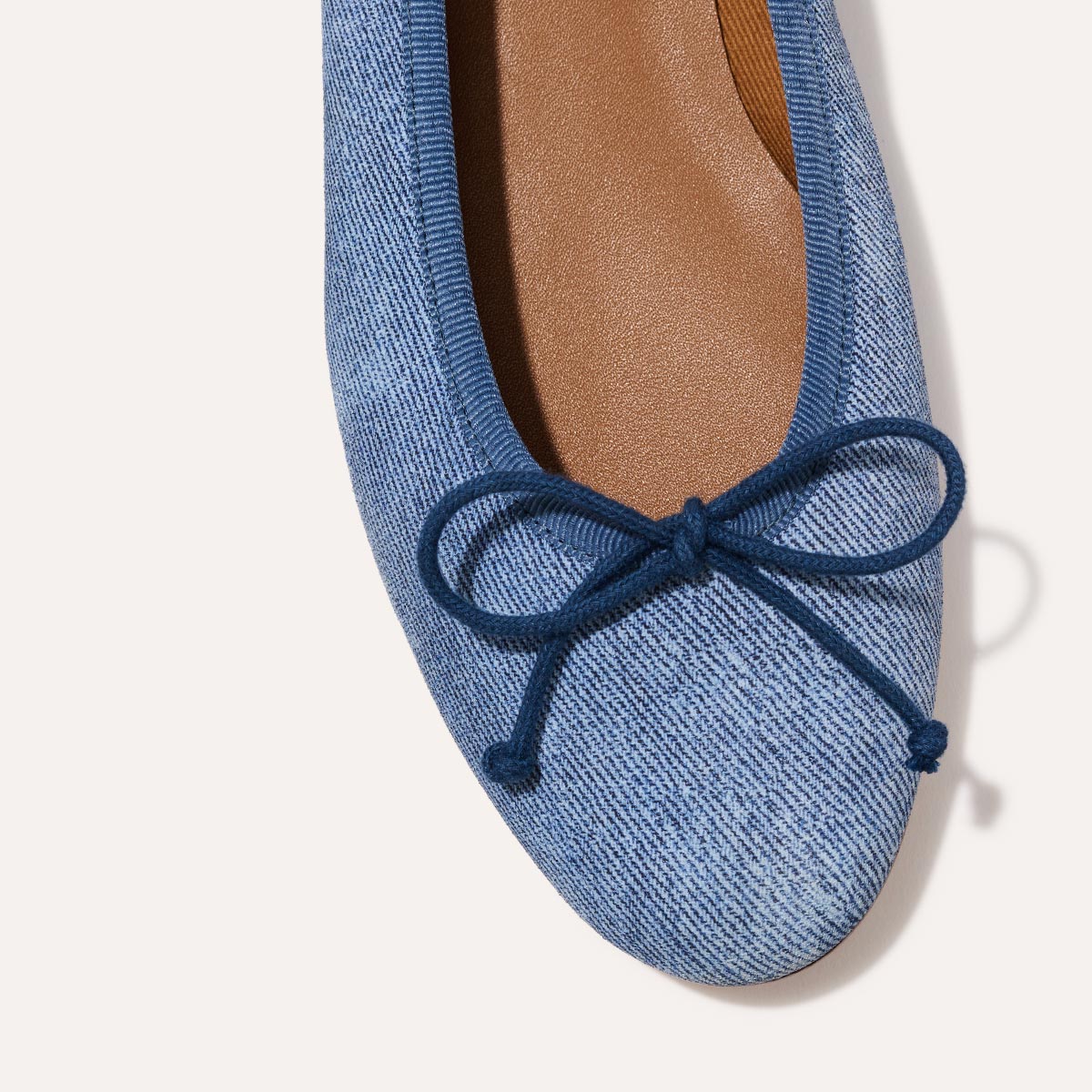 The Demi in soft Denim Suede, a comfortable ballet flat with a rounded toe and adjustable cord bow detail.