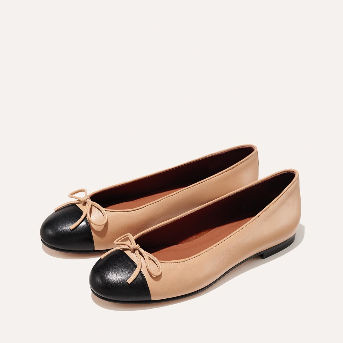 The Demi in Dune Nappa with a black cap-toe detail, a comfortable ballet flat with a rounded toe and adjustable cord bow detail.