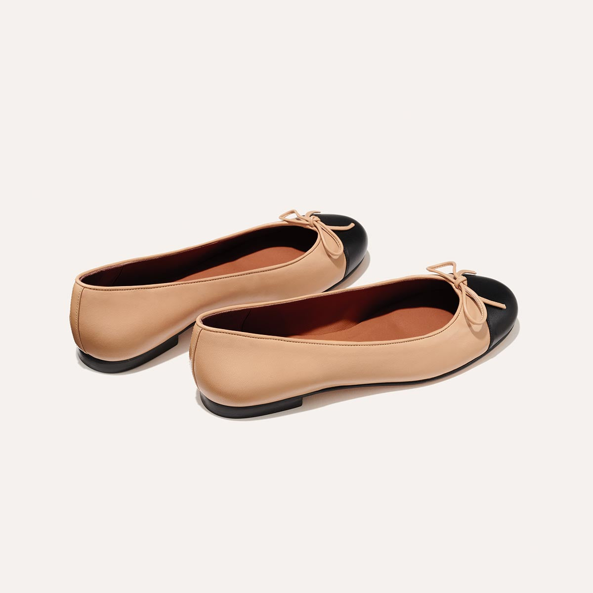 The Demi in Dune Nappa with a black cap-toe detail, a comfortable ballet flat with a rounded toe and adjustable cord bow detail.