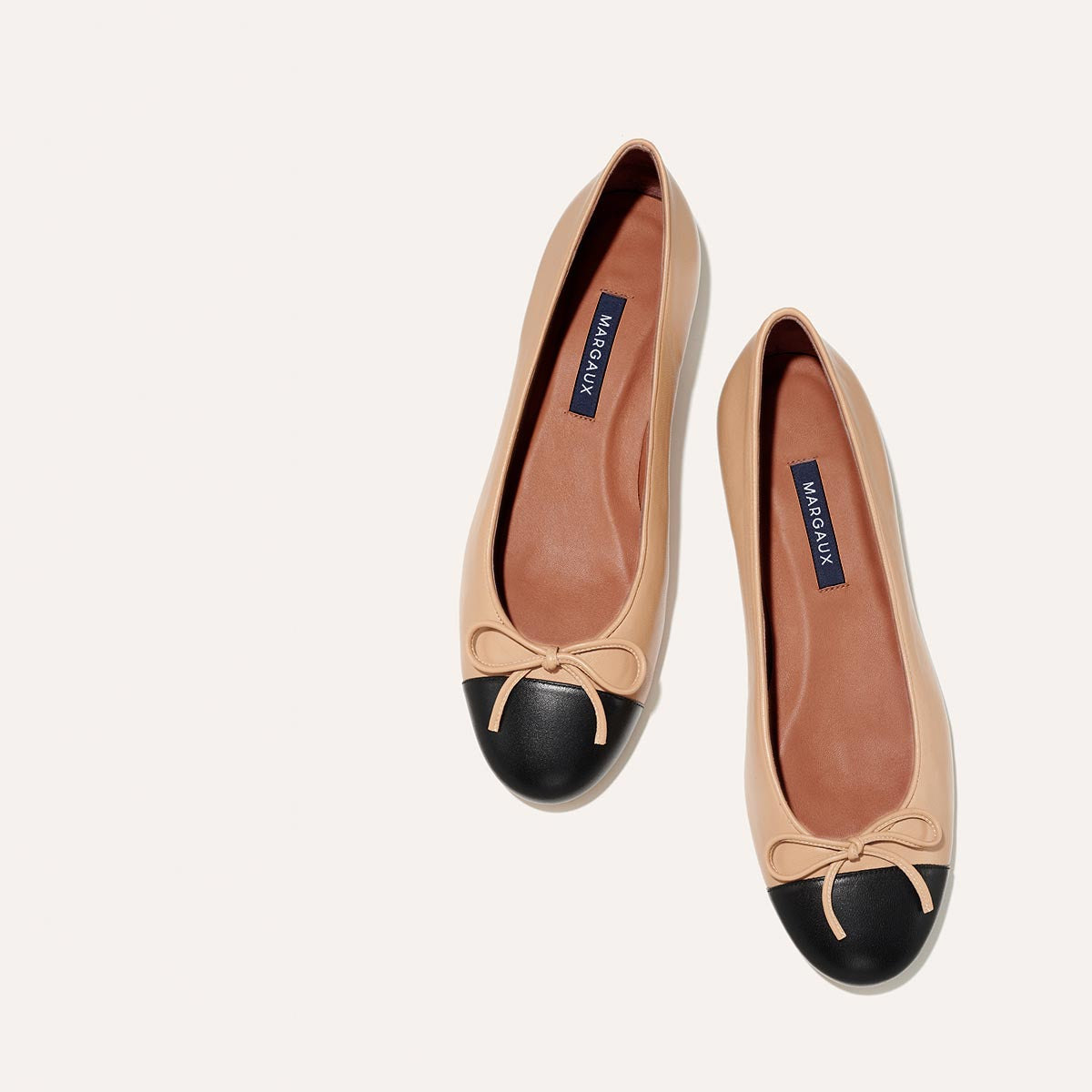 The Demi in Dune Nappa with a black cap-toe detail, a comfortable ballet flat with a rounded toe and adjustable cord bow detail.