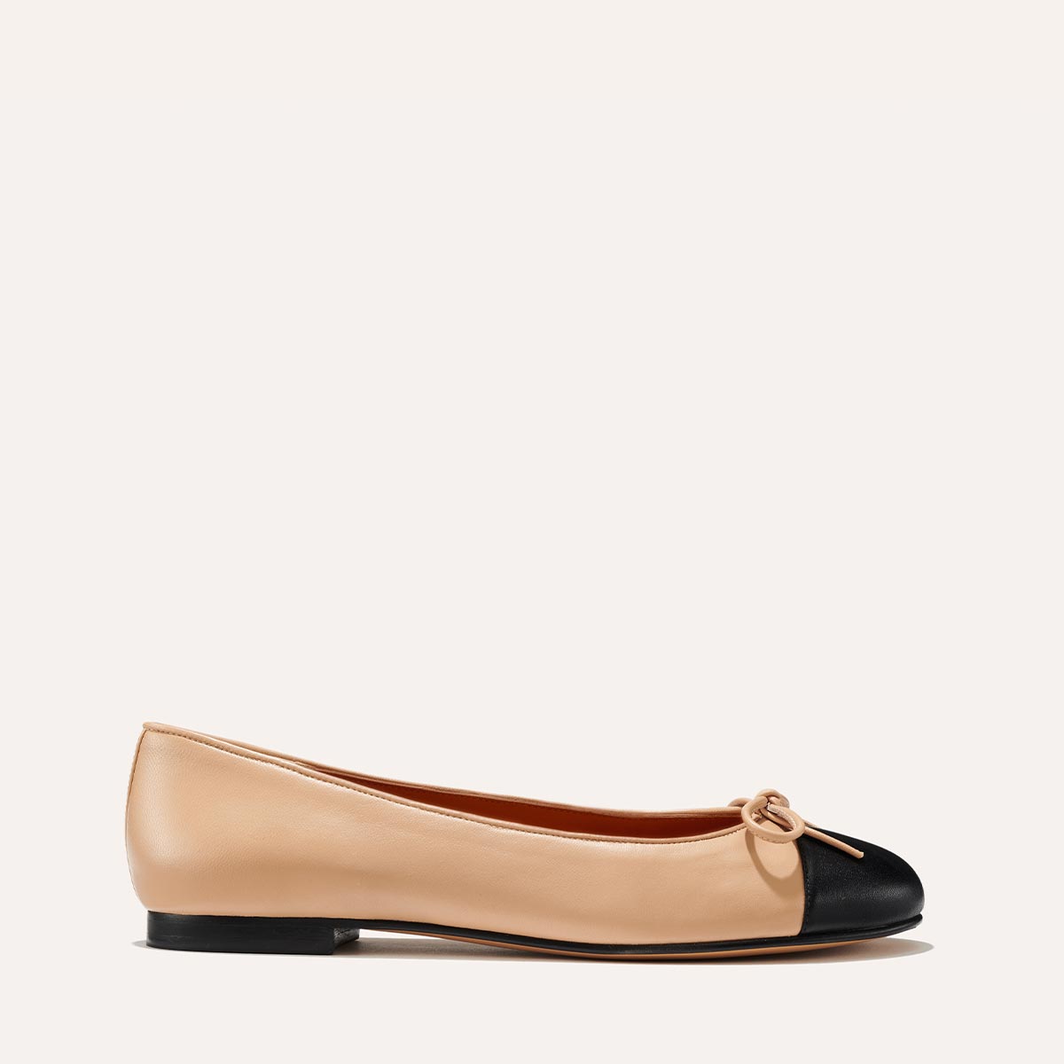 The Demi in Dune Nappa with a black cap-toe detail, a comfortable ballet flat with a rounded toe and adjustable cord bow detail.