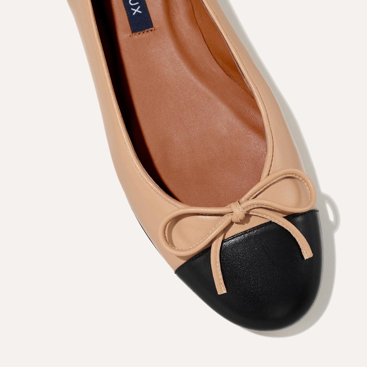 The Demi in Dune Nappa with a black cap-toe detail, a comfortable ballet flat with a rounded toe and adjustable cord bow detail.