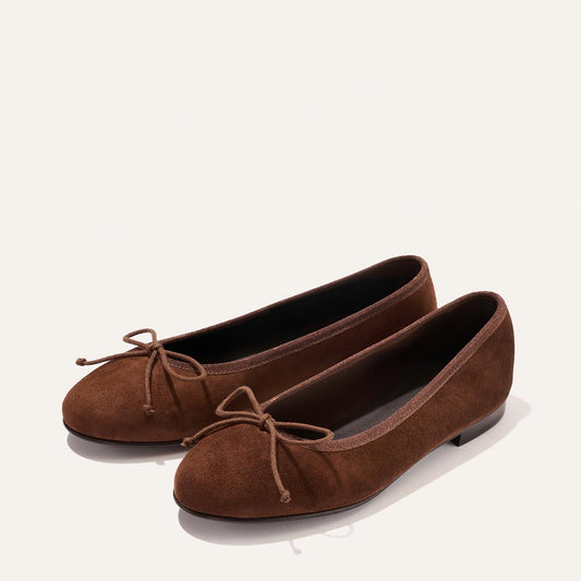 A pair of The Demi - Ganache Suede ballet flats by Margaux, handcrafted in Spain from brown suede and adorned with small front bows, displayed on a plain light background.