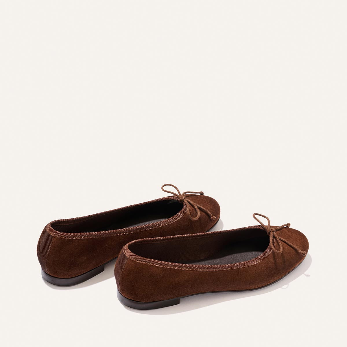 A pair of The Demi - Ganache Suede ballet flats by Margaux, featuring comfortable brown suede and small bows on the front, handmade in Spain and displayed on a light background.