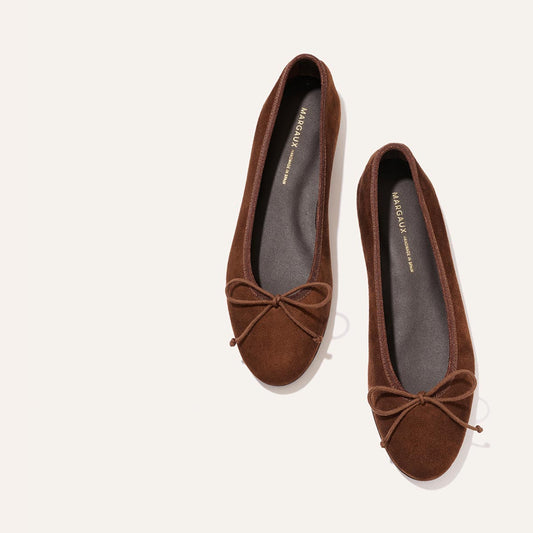 A pair of The Demi - Ganache Suede ballet flats by Margaux, crafted from brown suede and featuring bow details on the toes, are handmade in Spain and placed side by side on a light background.
