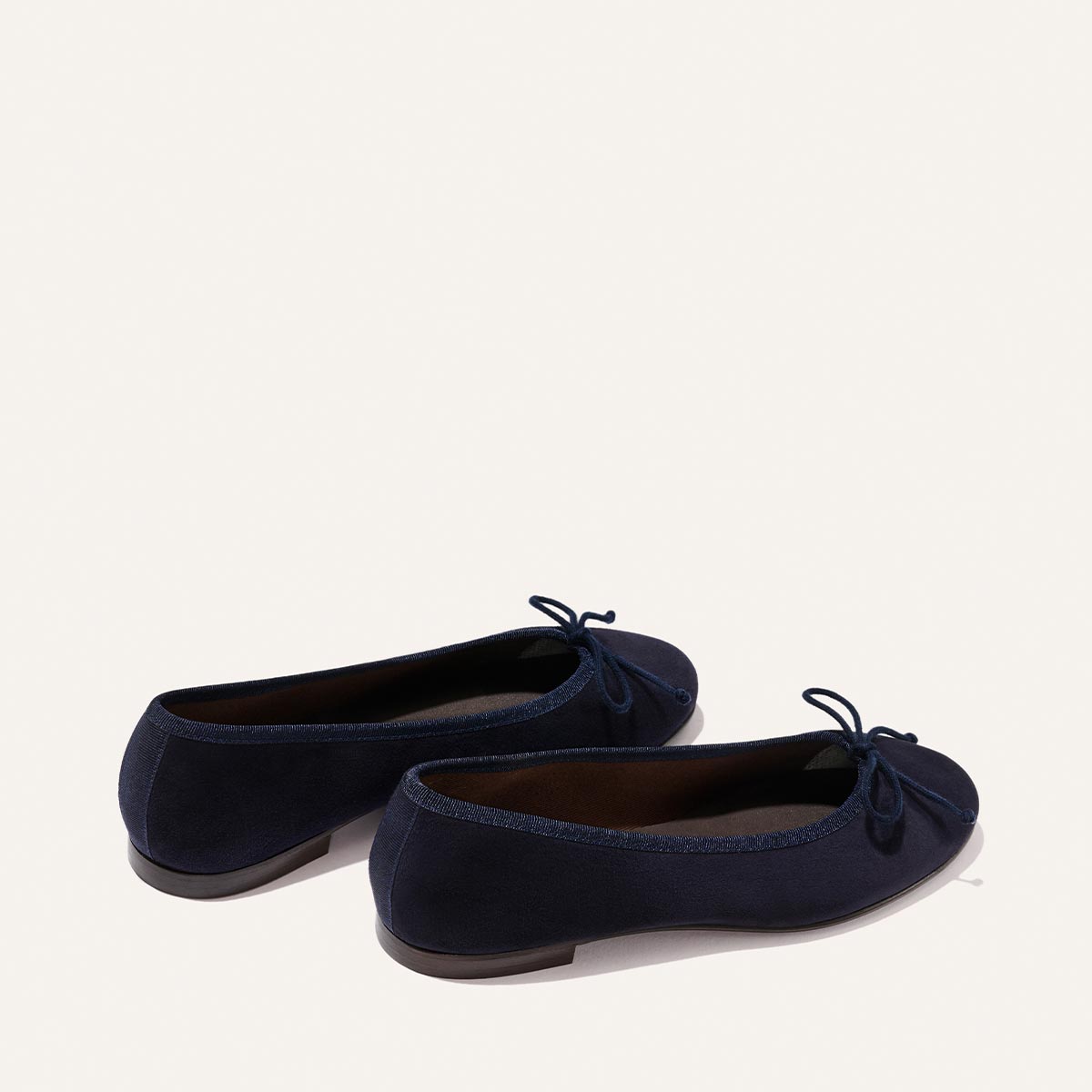 The Demi - Indigo Suede by Margaux are comfortable navy suede ballet flats with small bows, rounded toes, and low heels, handmade in Spain and shown on a light background.