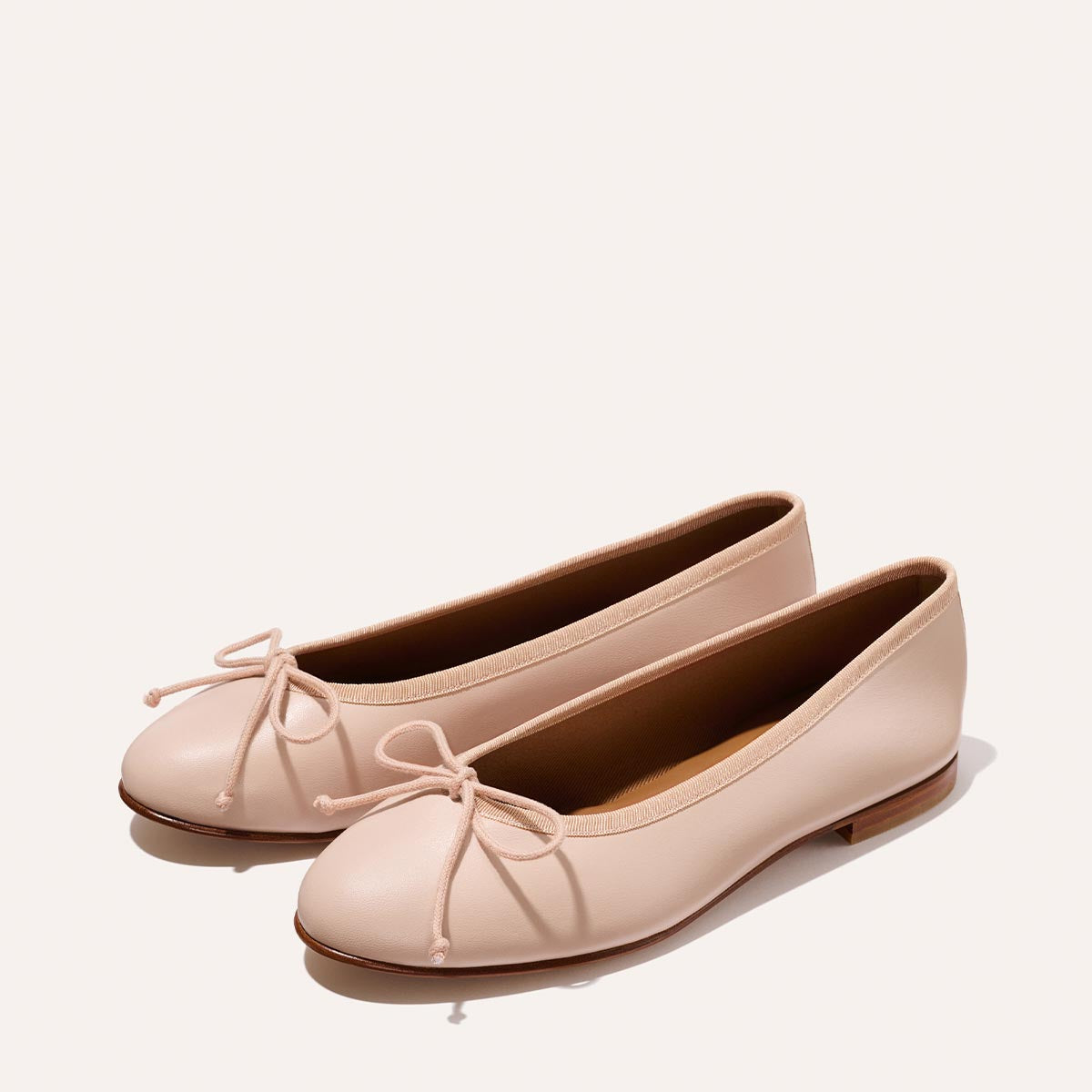 The Demi - Petal Nappa by Margaux: light pink ballet flats with rounded toes, dainty front bows, and low brown soles. Handmade in Spain and shown on a neutral background.