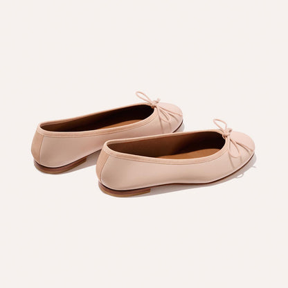 The Demi - Petal Nappa by Margaux: light pink ballet flats handmade in Spain, featuring small bows on the toes, shown on a plain off-white background.