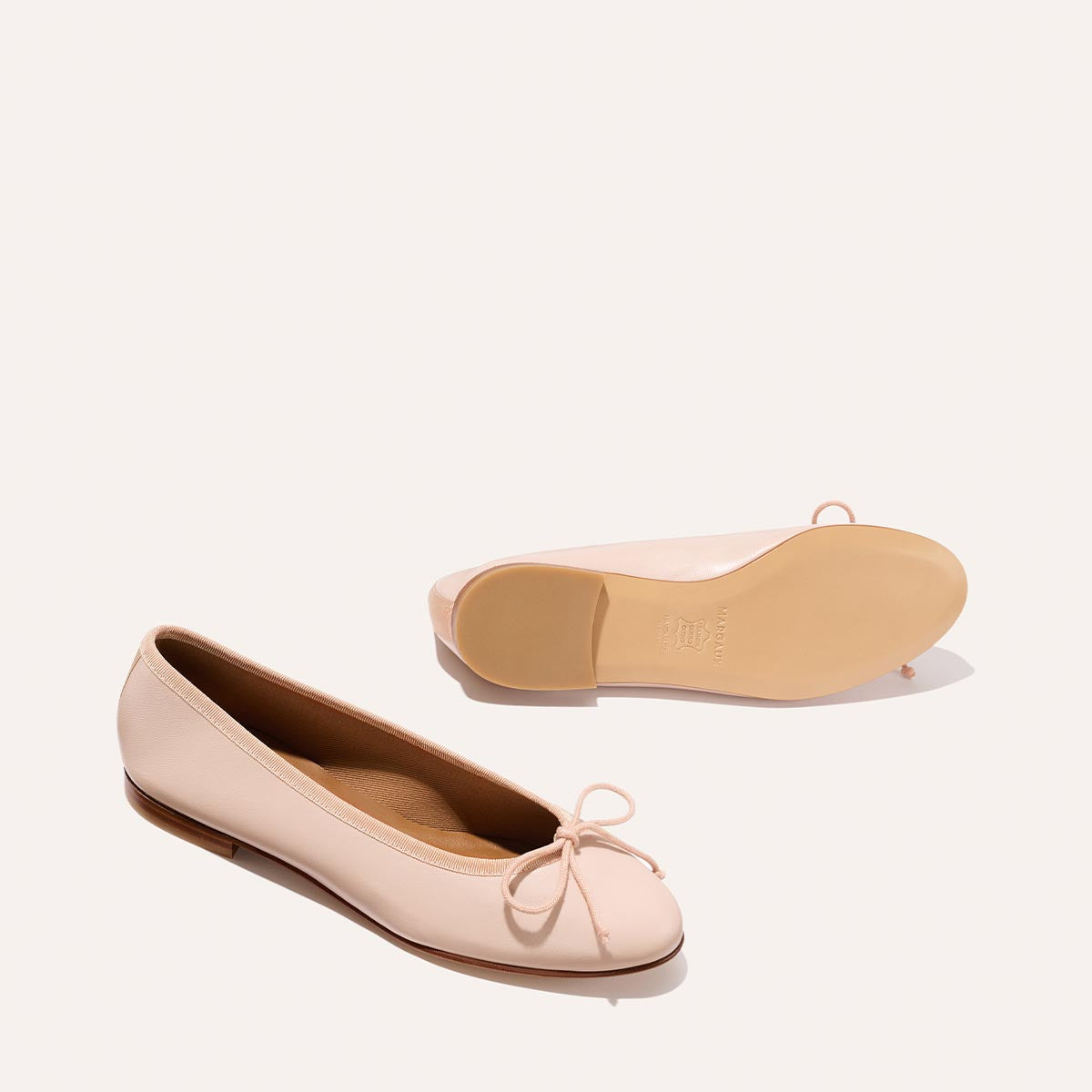 The Demi - Petal Nappa by Margaux: Handmade in Spain, these pale pink ballet flats feature a small toe bow and smooth sole—one shoe upright, one on its side. Perfect for everyday elegance and comfort.
