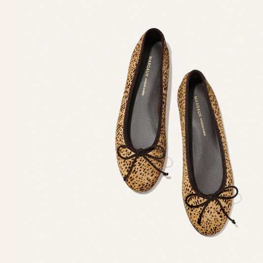 Top view of The Demi - Tan Mini Cheetah Haircalf ballet flats by Margaux, handmade in Spain, featuring black trim and bows, displayed on a white background. The gray insoles with gold text add a touch of style and comfort.