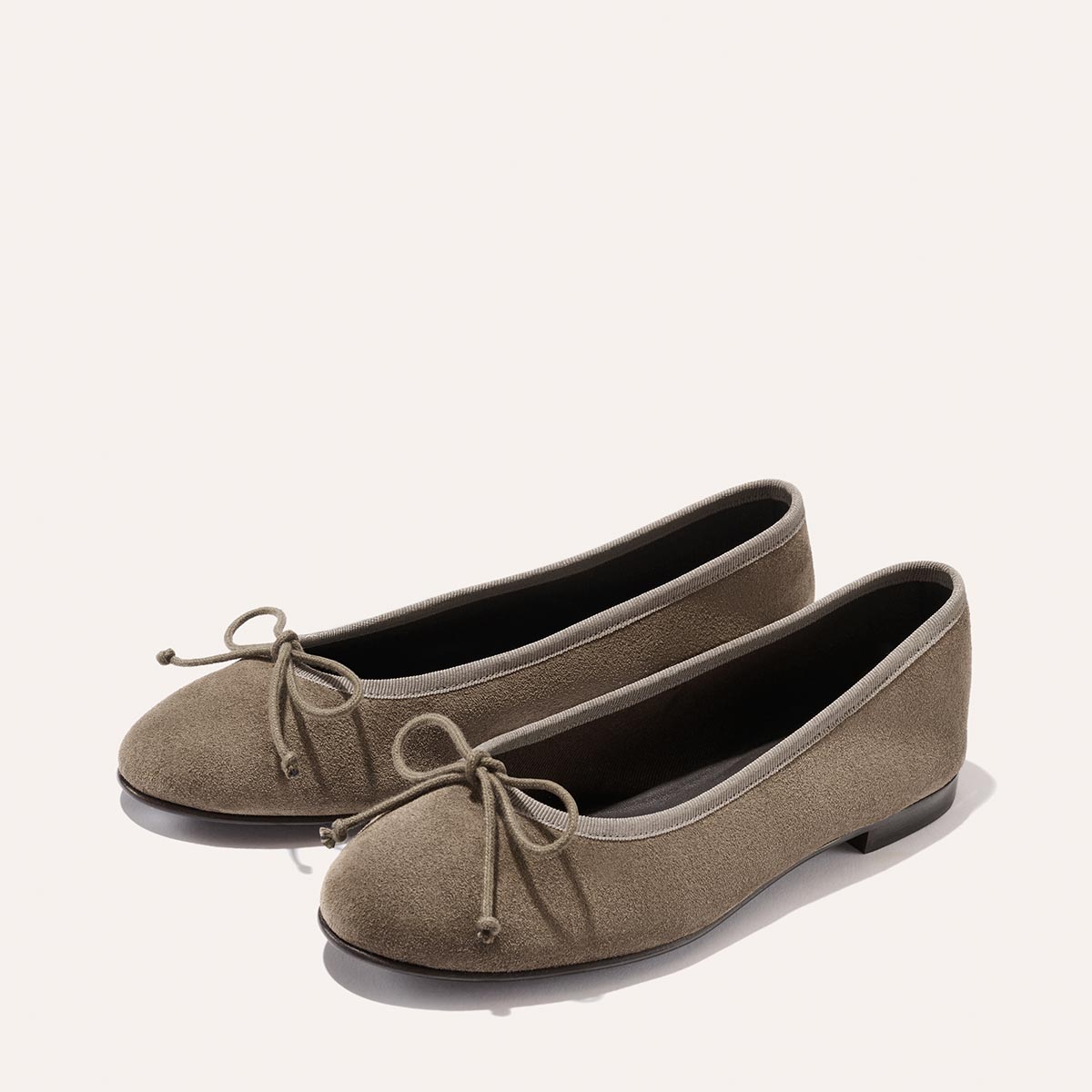 The Demi - Truffle Suede by Margaux: taupe suede ballet flats, handmade in Spain with rounded toes and decorative bows, displayed on a plain light background.