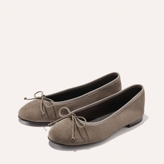 The Demi - Truffle Suede by Margaux, a pair of handmade taupe suede ballet flats featuring a bow detail on the toe, are photographed against a plain light background.
