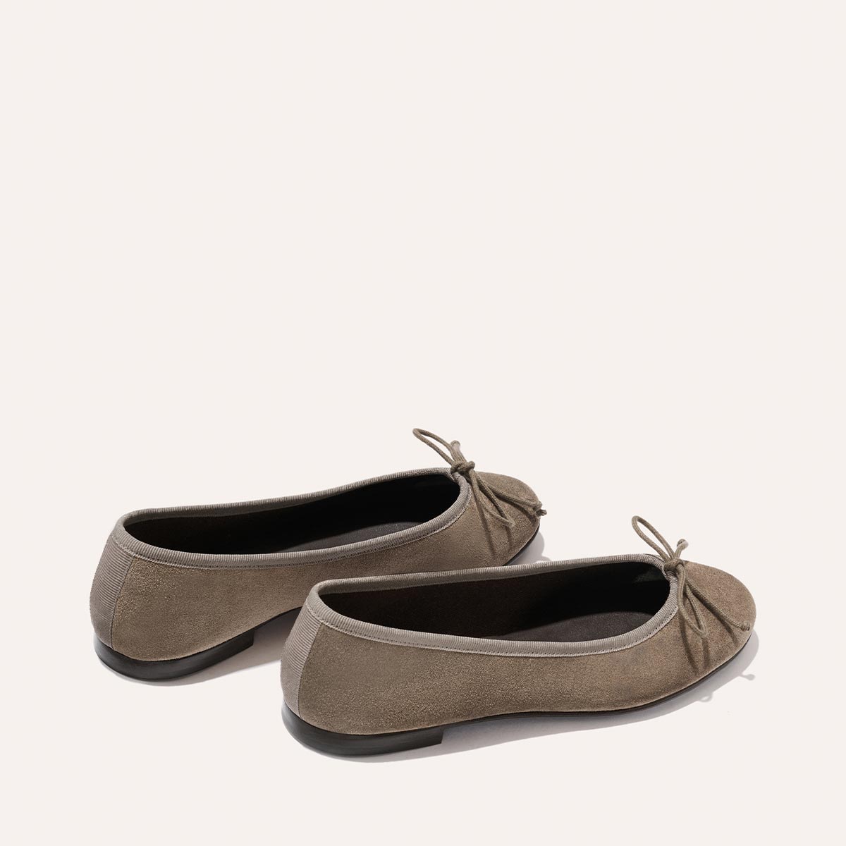 The Demi - Truffle Suede by Margaux: taupe suede ballet flats, handmade in Spain with rounded toes, front bows, and black soles, displayed on a light background.