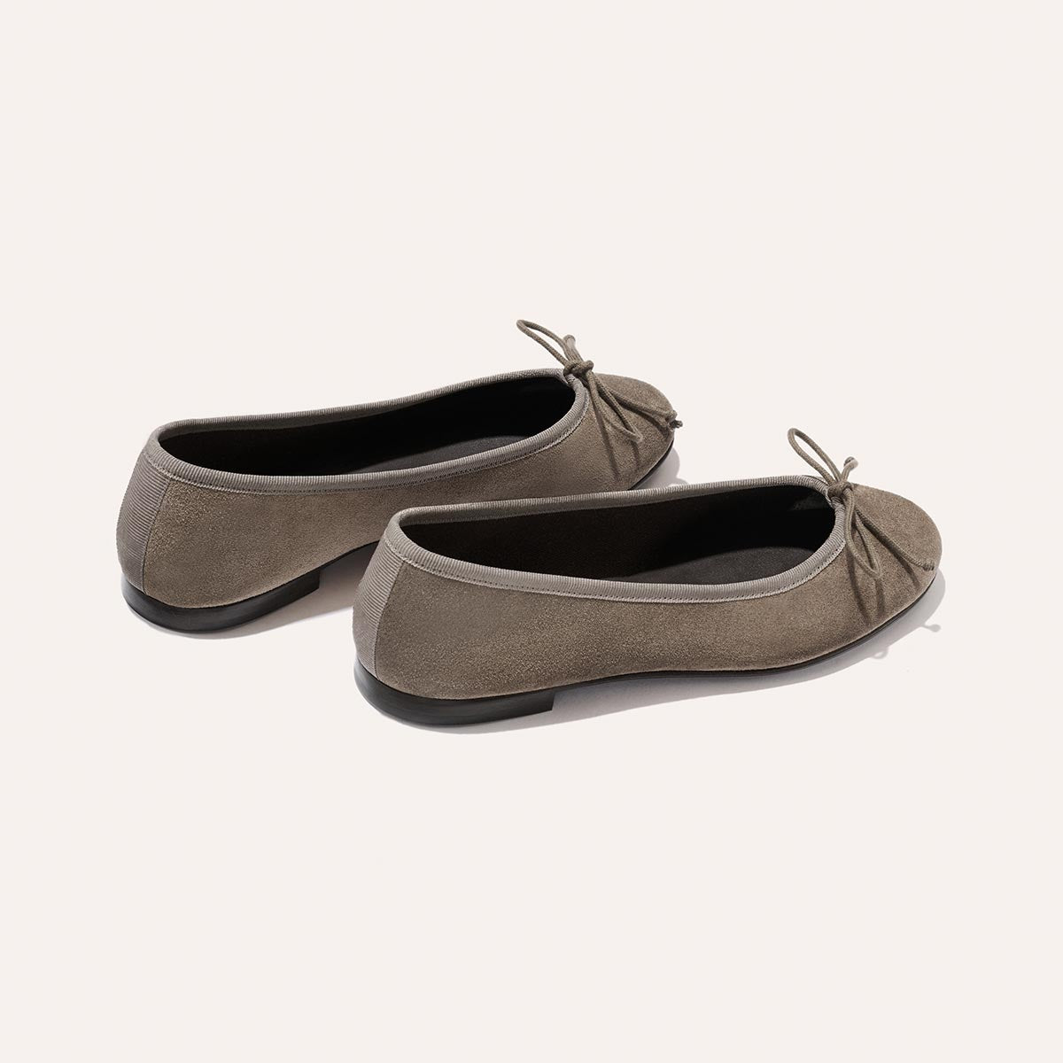 The Demi - Truffle Suede by Margaux are handmade ballet flats in taupe suede, adorned with petite bows on the front and displayed against a light background.