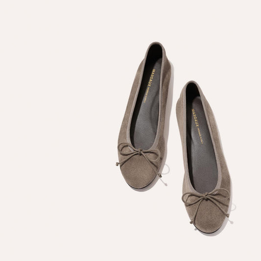A pair of Margaux’s The Demi - Truffle Suede ballet flats, handmade in Spain from taupe suede with delicate bows on the toes and designed for comfortable all-day wear, displayed on a plain light background.