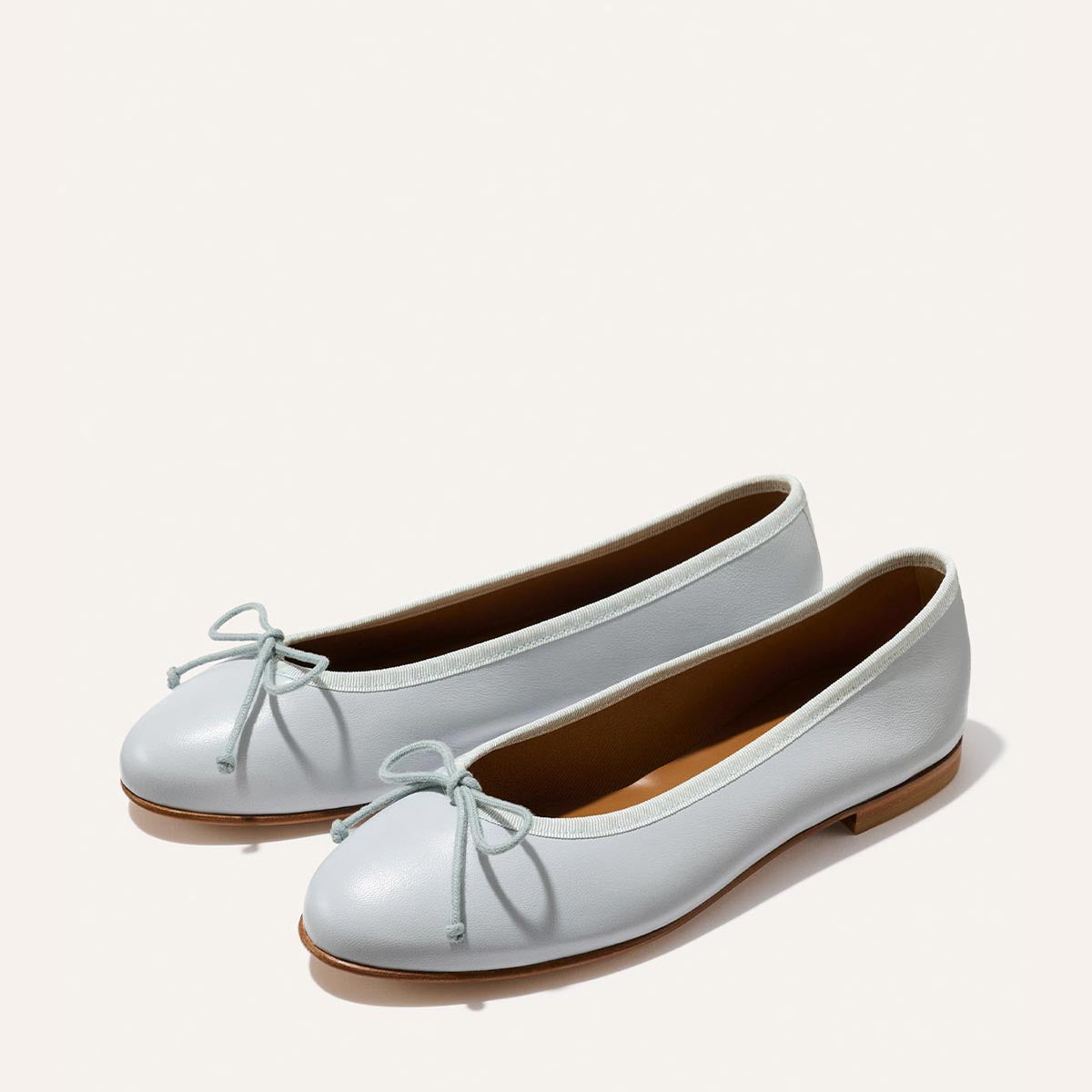 The Demi - Mist Blue Nappa by Margaux: light blue ballet flats handmade in Spain, feature small toe bows, tan lining, and flat brown soles. Artisanal craftsmanship and comfort in every pair, shown side by side on a plain light background.