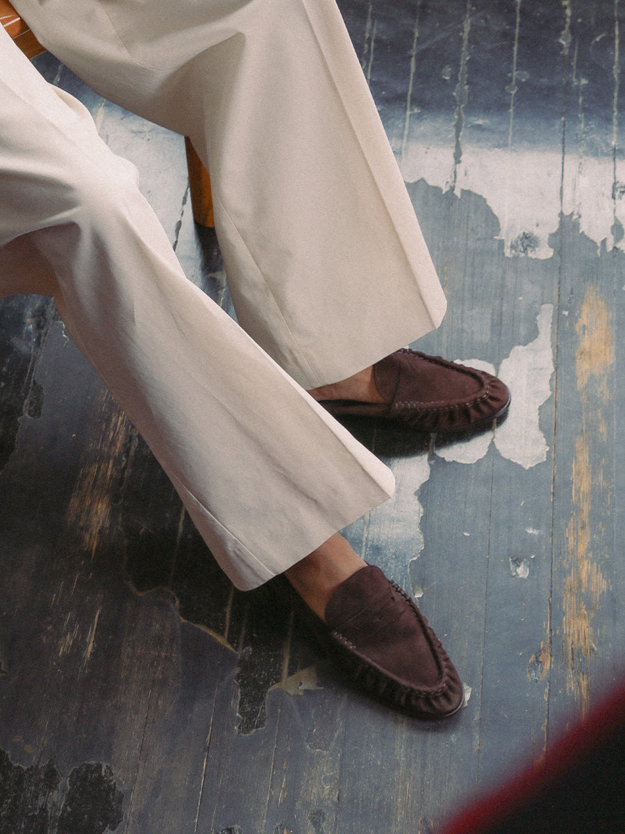 Person wearing white pants and brown loafers on a textured blue floor.