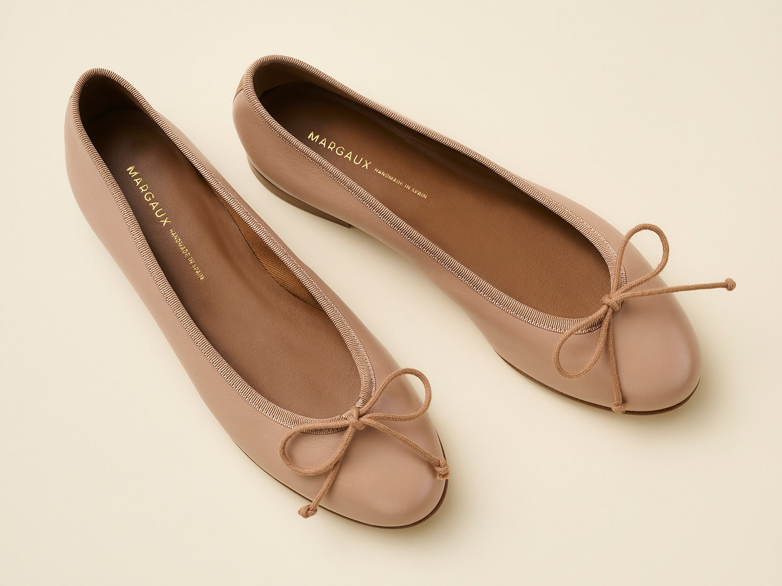 Pair of beige ballet flats with bow details on a light background