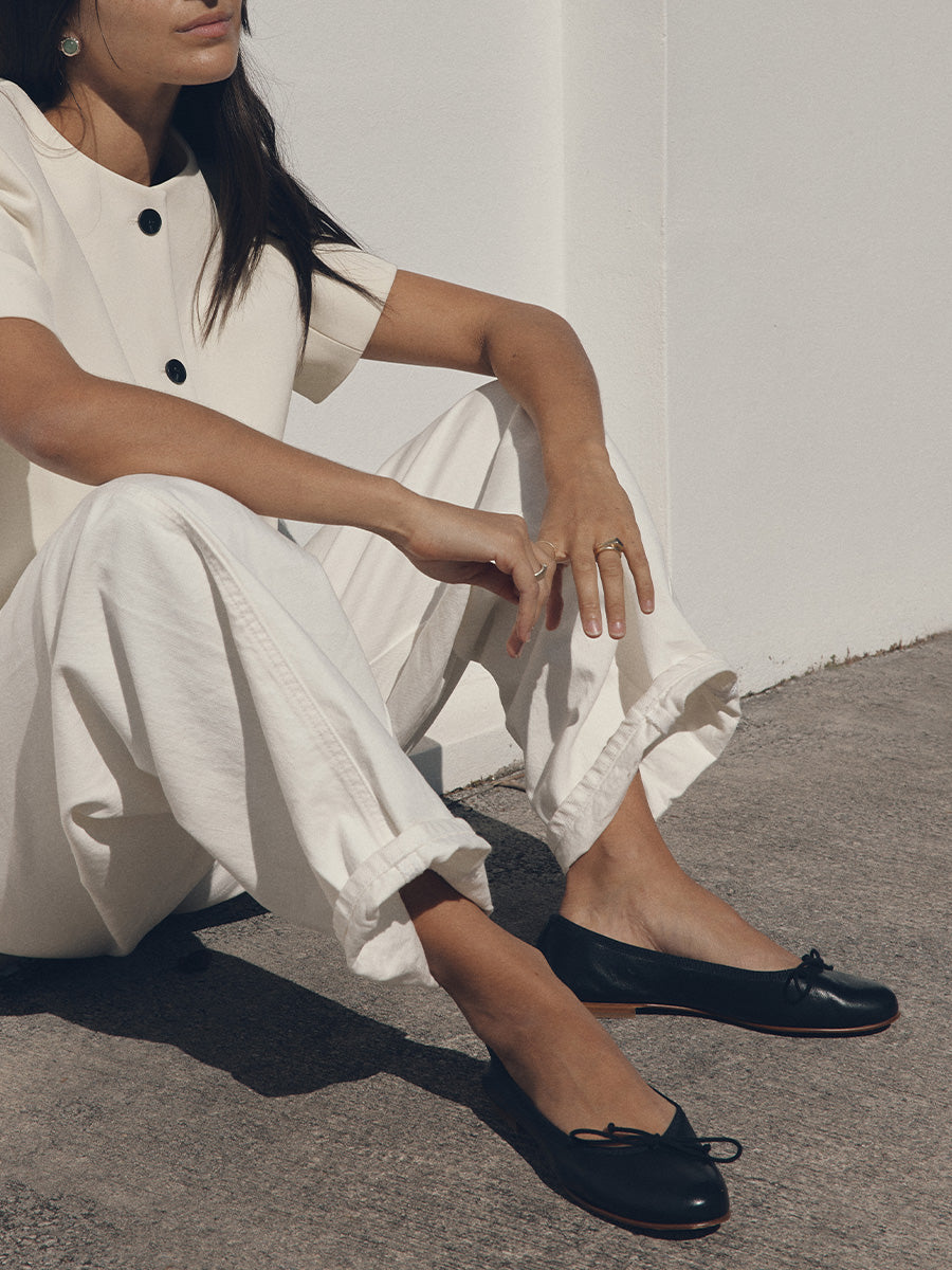 Person wearing a white outfit with black shoes sitting on a concrete surface.