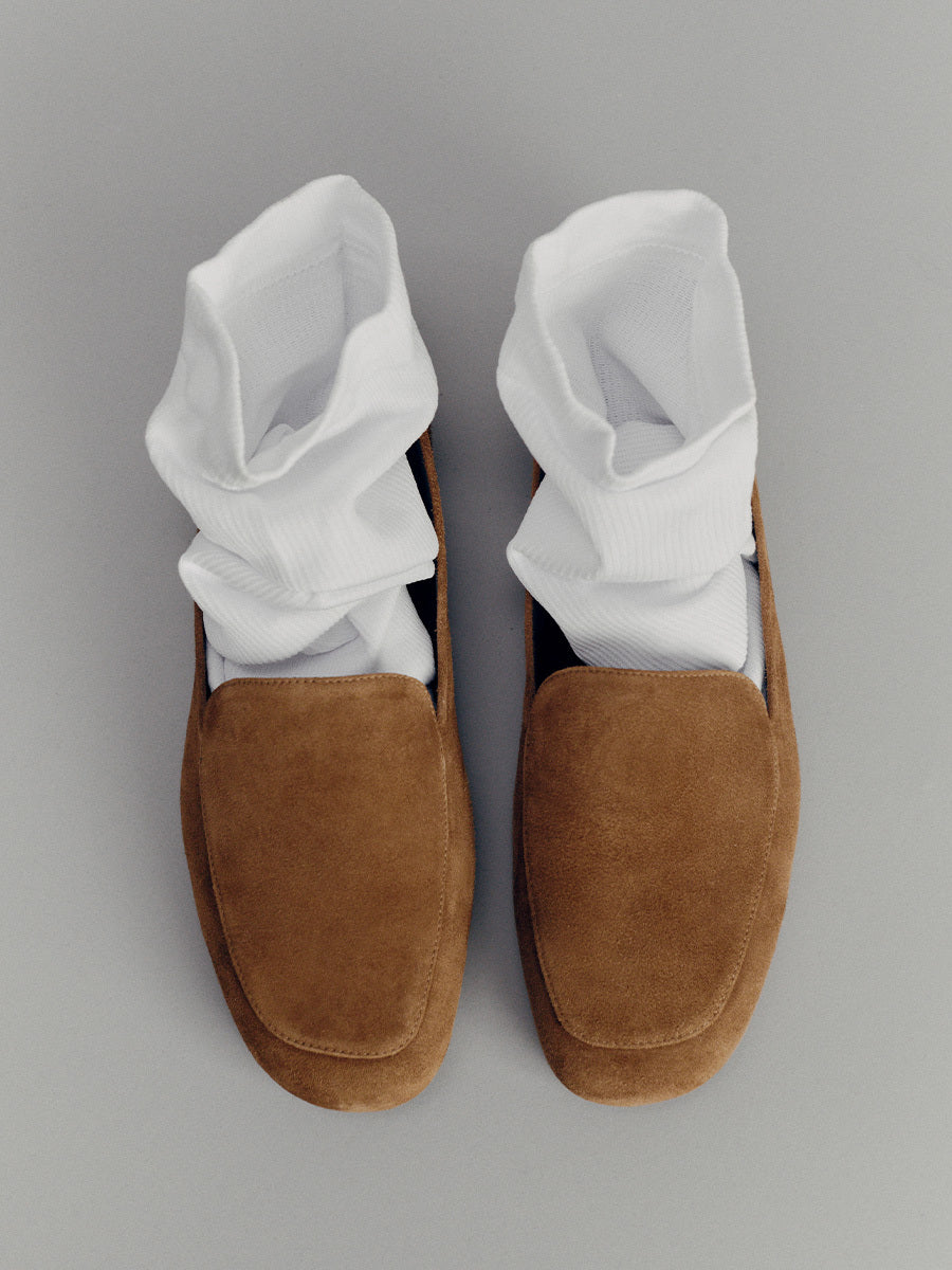 Brown loafers with white socks on a gray background