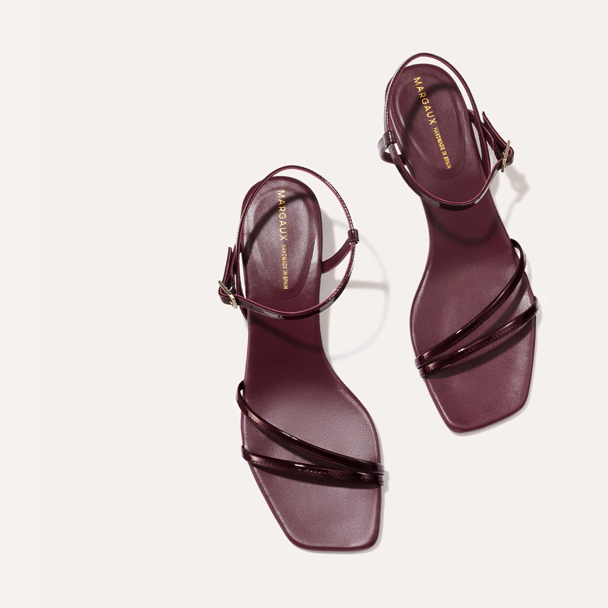 The Dylan Sandal in shiny Burgundy Patent, featuring asymmetrical straps around the ankle and toes and a walkable 1-inch stiletto heel.