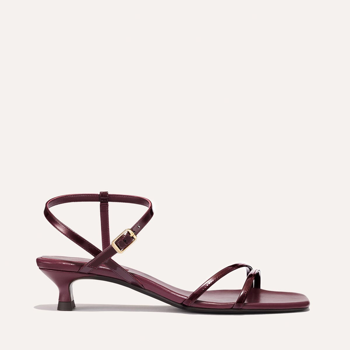 The Dylan Sandal in shiny Burgundy Patent, featuring asymmetrical straps around the ankle and toes and a walkable 1-inch stiletto heel.