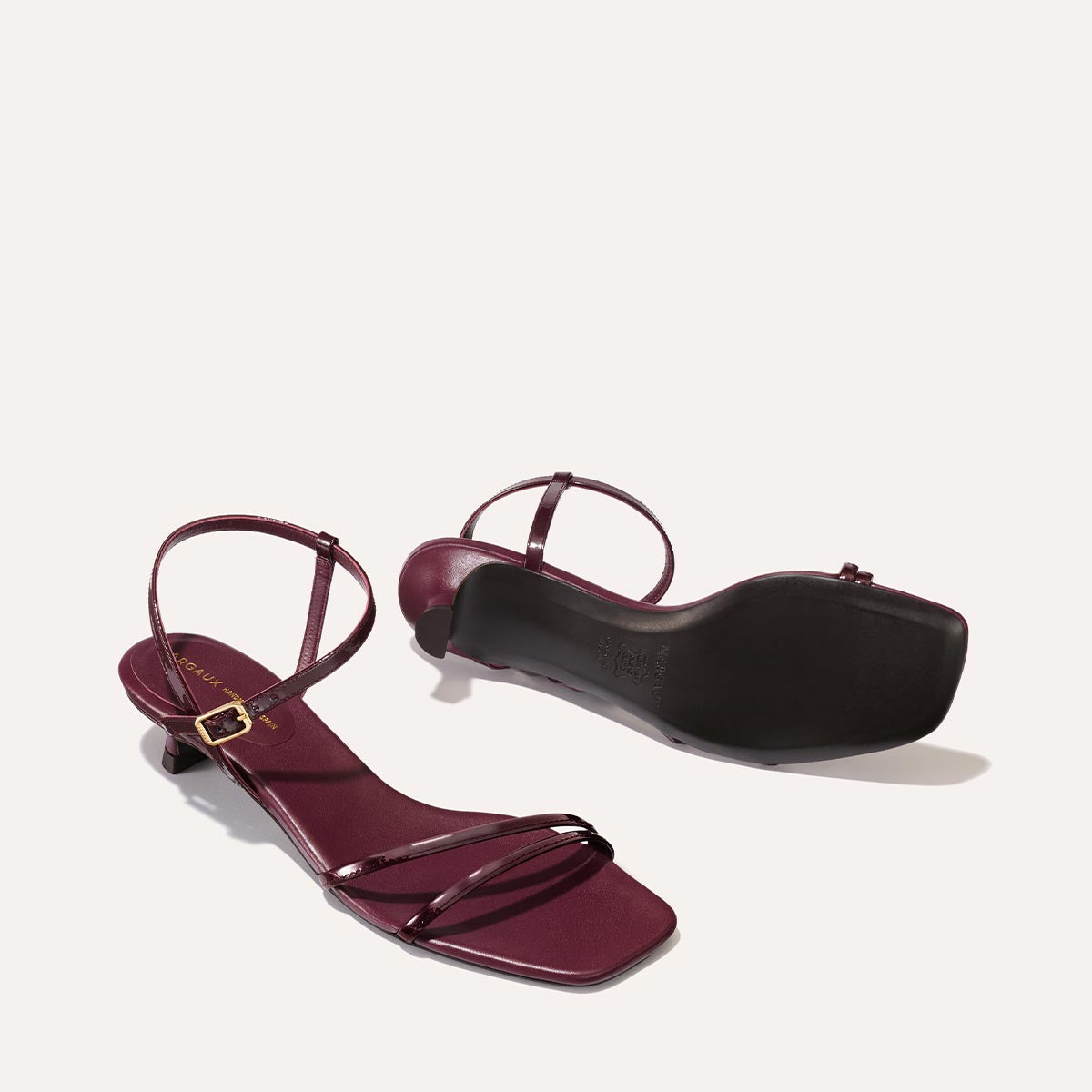 The Dylan Sandal in shiny Burgundy Patent, featuring asymmetrical straps around the ankle and toes and a walkable 1-inch stiletto heel.