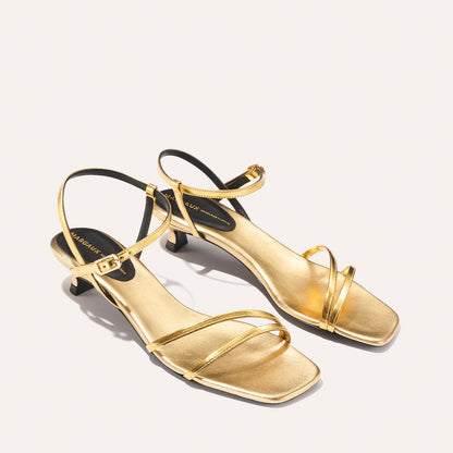 The Dylan Sandal - Gold Mirror by margaux-development: gold strappy heeled sandals with square toes, small heels, ankle straps, and a minimalist design shown on a light background.