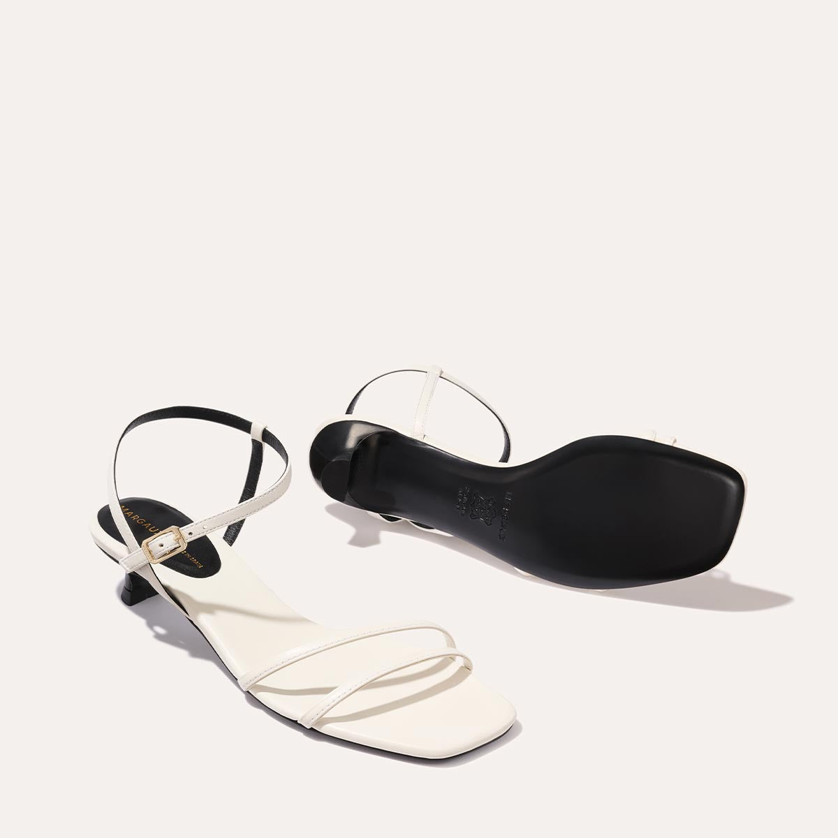 The Dylan Sandal in Ivory Nappa, featuring asymmetrical straps around the ankle and toes and a walkable 1-inch stiletto heel.