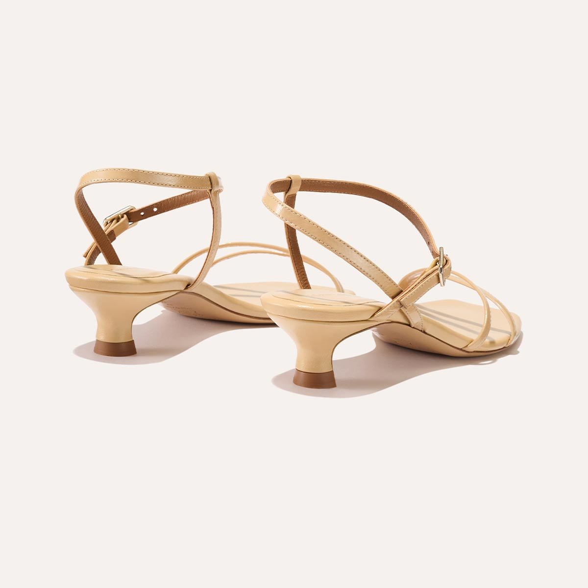 The Dylan Sandal in shiny Sand Crinkle-Gloss Nappa, featuring asymmetrical straps around the ankle and toes and a walkable 1-inch stiletto heel.