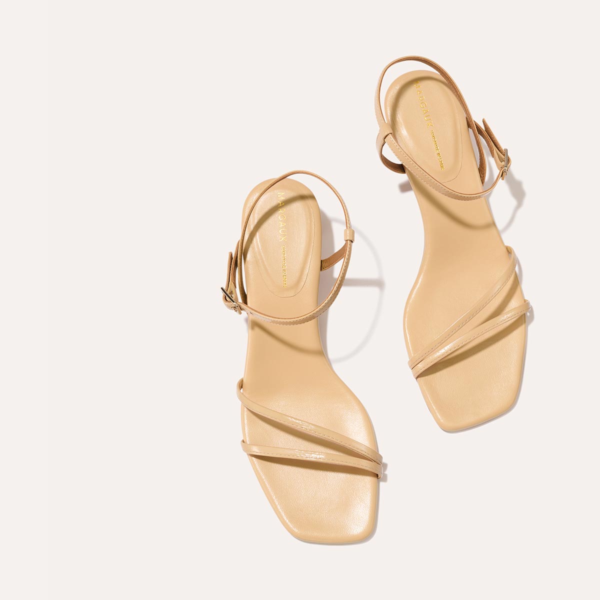 The Dylan Sandal in shiny Sand Crinkle-Gloss Nappa, featuring asymmetrical straps around the ankle and toes and a walkable 1-inch stiletto heel.