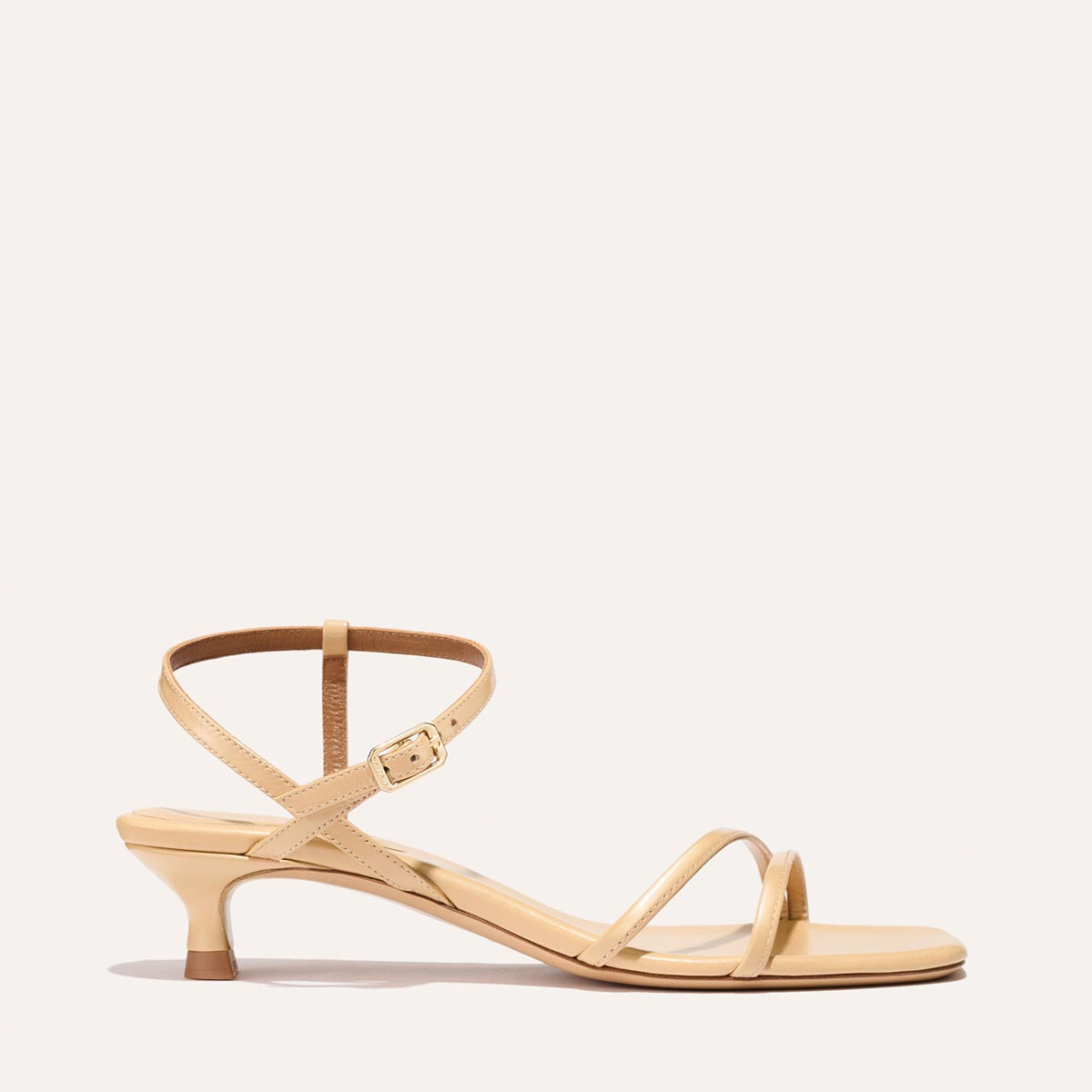 The Dylan Sandal in shiny Sand Crinkle-Gloss Nappa, featuring asymmetrical straps around the ankle and toes and a walkable 1-inch stiletto heel.