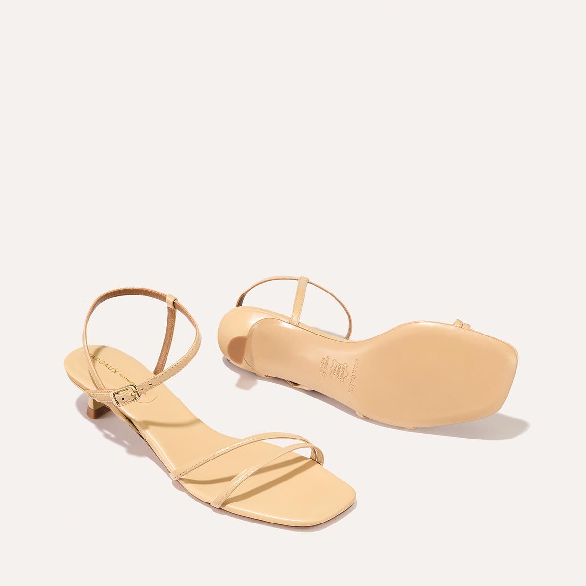 The Dylan Sandal in shiny Sand Crinkle-Gloss Nappa, featuring asymmetrical straps around the ankle and toes and a walkable 1-inch stiletto heel.