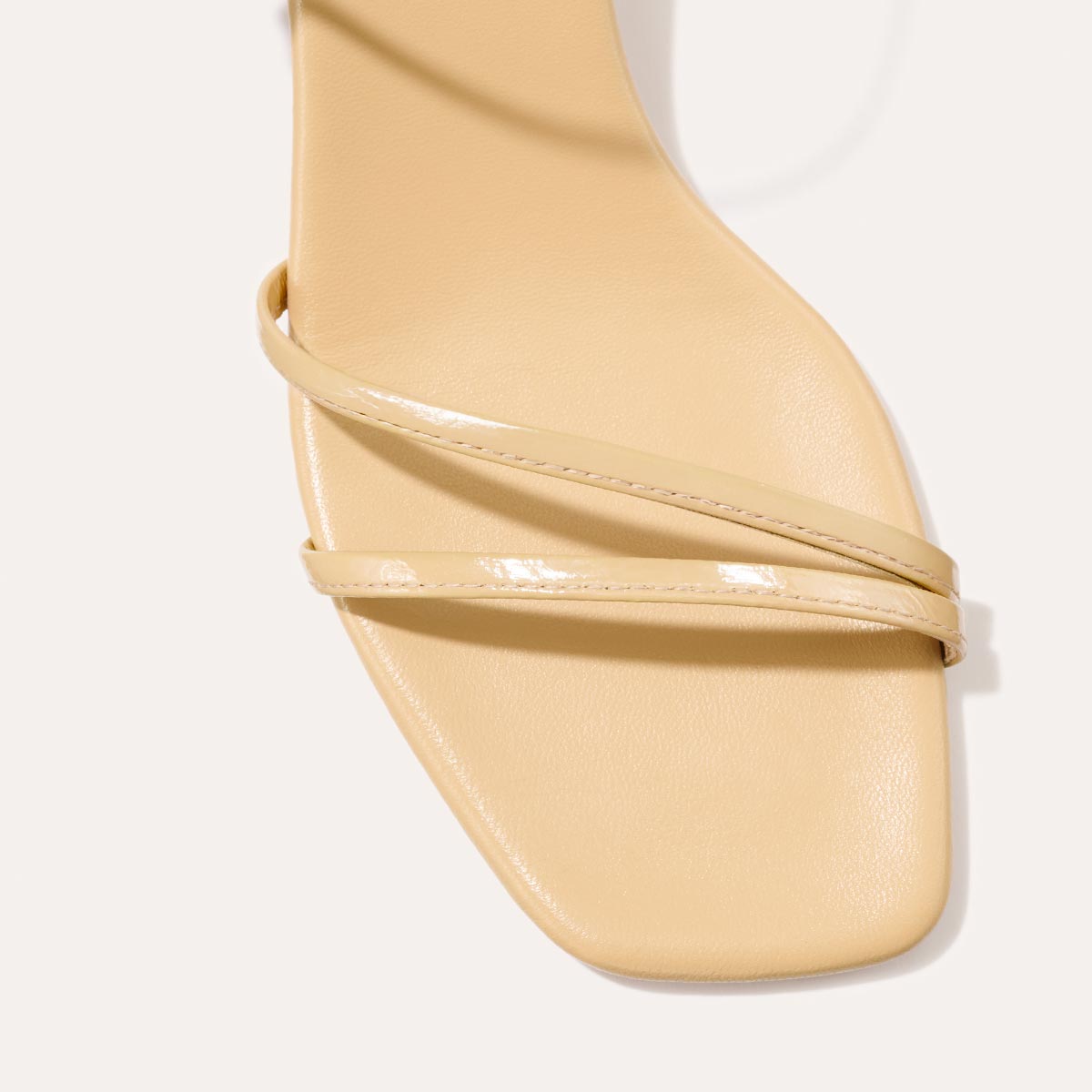 The Dylan Sandal in shiny Sand Crinkle-Gloss Nappa, featuring asymmetrical straps around the ankle and toes and a walkable 1-inch stiletto heel.