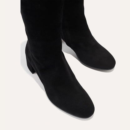 The Edie Boot in Black Suede, a sleek knee-high silhouette complemented by a comfortable 2.5-inch block heel and a hidden interior zipper for a fitted look.