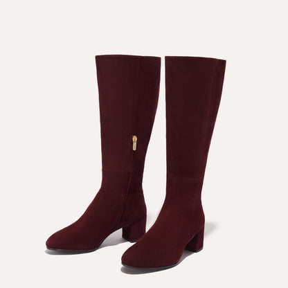 The Edie Boot in Burgundy Suede, a sleek knee-high silhouette complemented by a comfortable 2.5-inch block heel and a hidden interior zipper for a fitted look.
