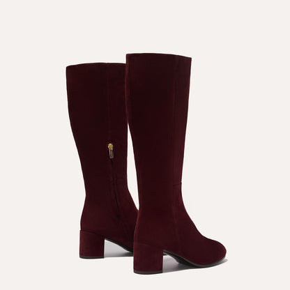 The Edie Boot in Burgundy Suede, a sleek knee-high silhouette complemented by a comfortable 2.5-inch block heel and a hidden interior zipper for a fitted look.