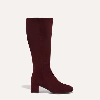 The Edie Boot in Burgundy Suede, a sleek knee-high silhouette complemented by a comfortable 2.5-inch block heel and a hidden interior zipper for a fitted look.