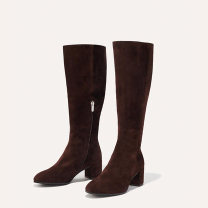 The Edie Boot in Chocolate Suede, a sleek knee-high silhouette complemented by a comfortable 2.5-inch block heel and a hidden interior zipper for a fitted look.