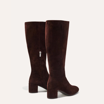 The Edie Boot in Chocolate Suede, a sleek knee-high silhouette complemented by a comfortable 2.5-inch block heel and a hidden interior zipper for a fitted look.