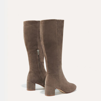 The Edie Boot in Taupe Suede, a sleek knee-high silhouette complemented by a comfortable 2.5-inch block heel and a hidden interior zipper for a fitted look.