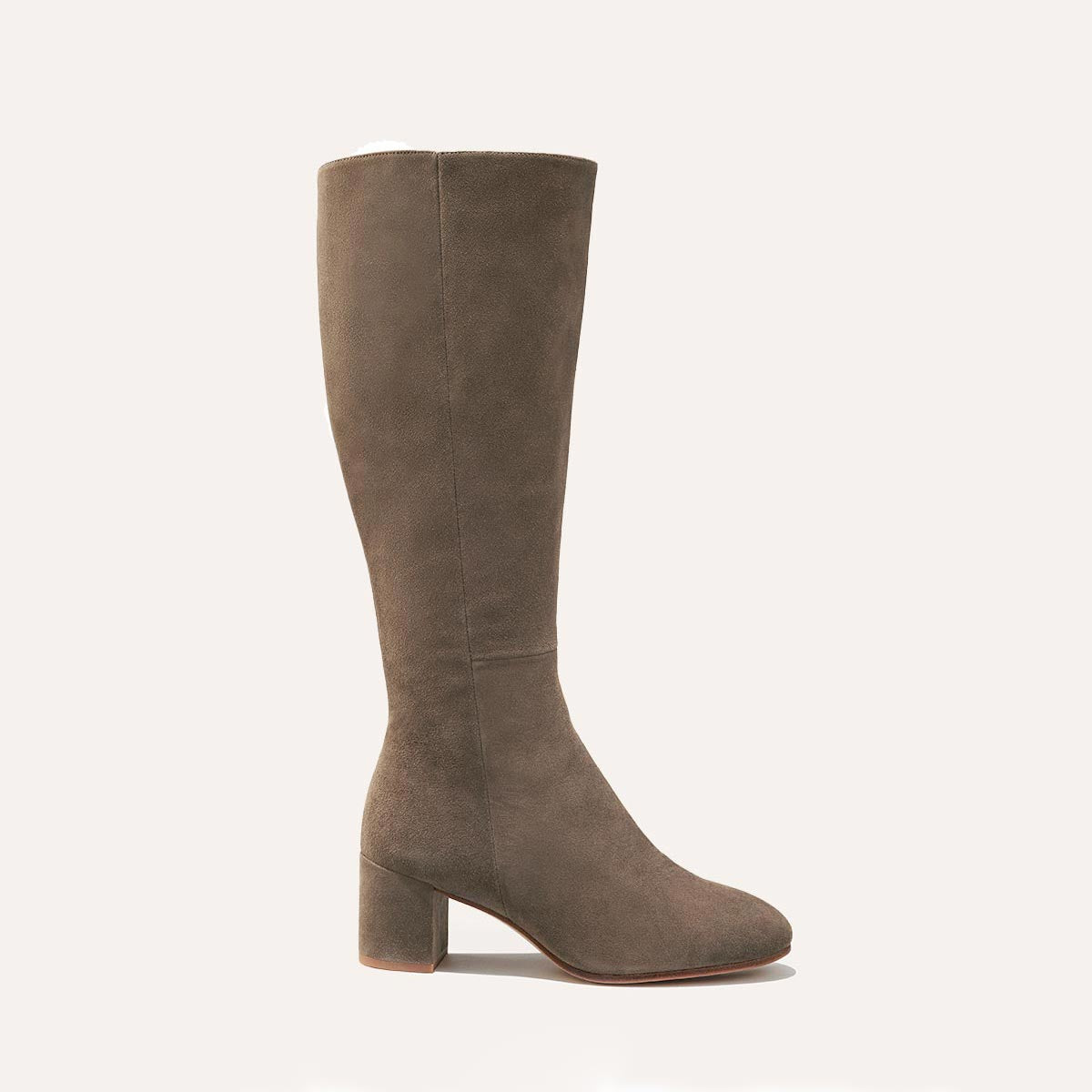 The Edie Boot in Taupe Suede, a sleek knee-high silhouette complemented by a comfortable 2.5-inch block heel and a hidden interior zipper for a fitted look.