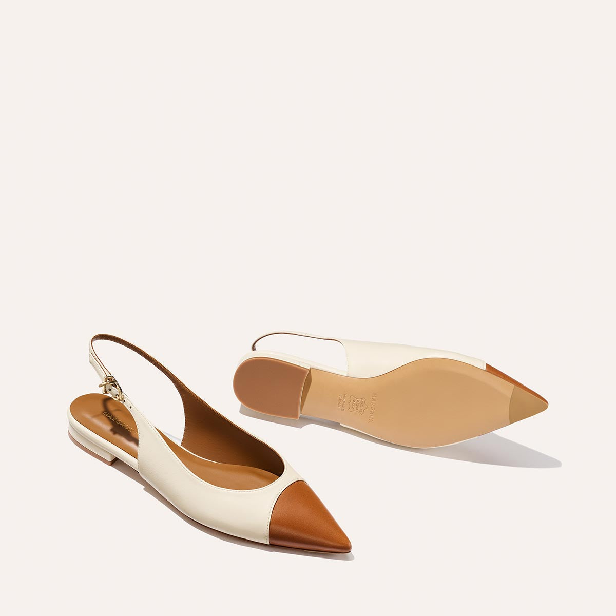 The Elise by margaux-development: women’s slingback flats in cream cotton with brown leather pointed toes, ankle straps, and gold buckles. One shoe is upright; the other shows the sole.