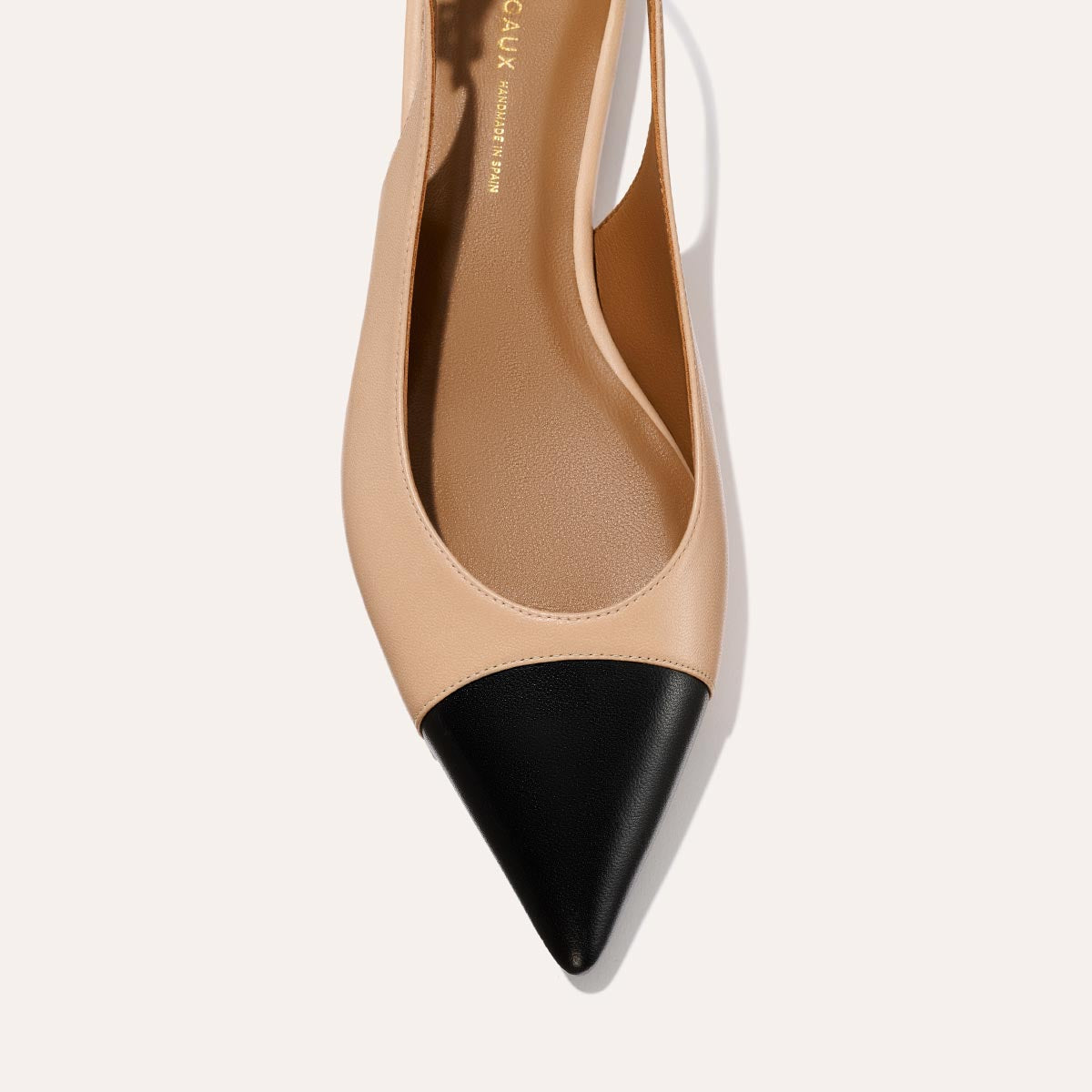 A close-up of The Elise - Dune and Black Nappa by margaux-development: a pointed-toe slingback with a beige body, black toe cap, and flat profile, shown against a neutral background.