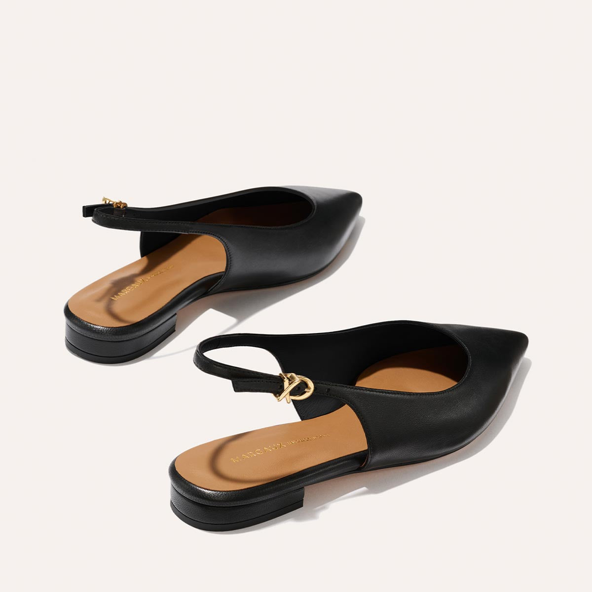 The Elise - Black Nappa by margaux-development: black pointed-toe slingback flats with low heels, tan insoles, and gold buckle accents, shown on a light background.