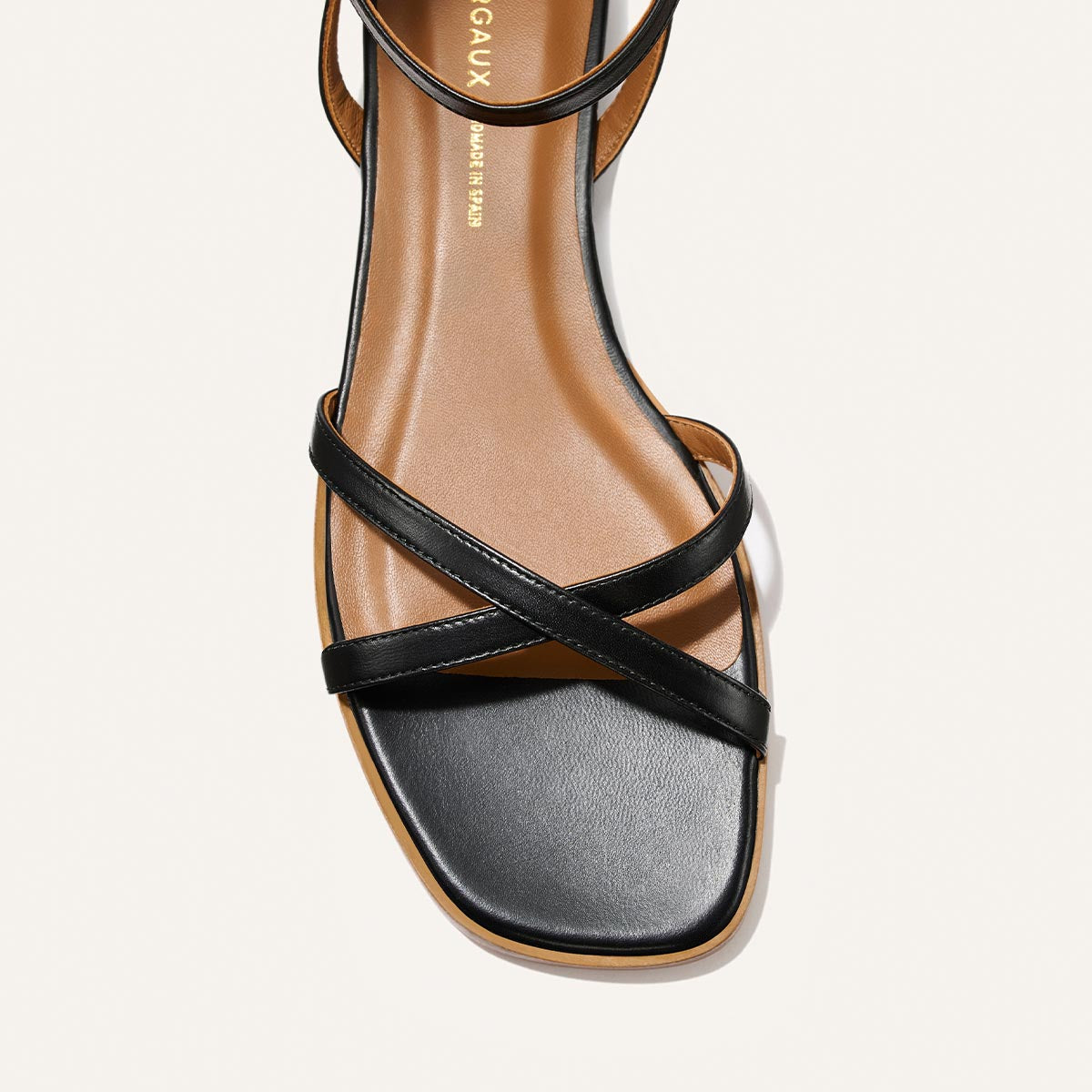 A close-up of Margaux’s The Flat Sandal - Black Nappa, featuring a square toe, tan footbed, and slim black leather straps for timeless style.
